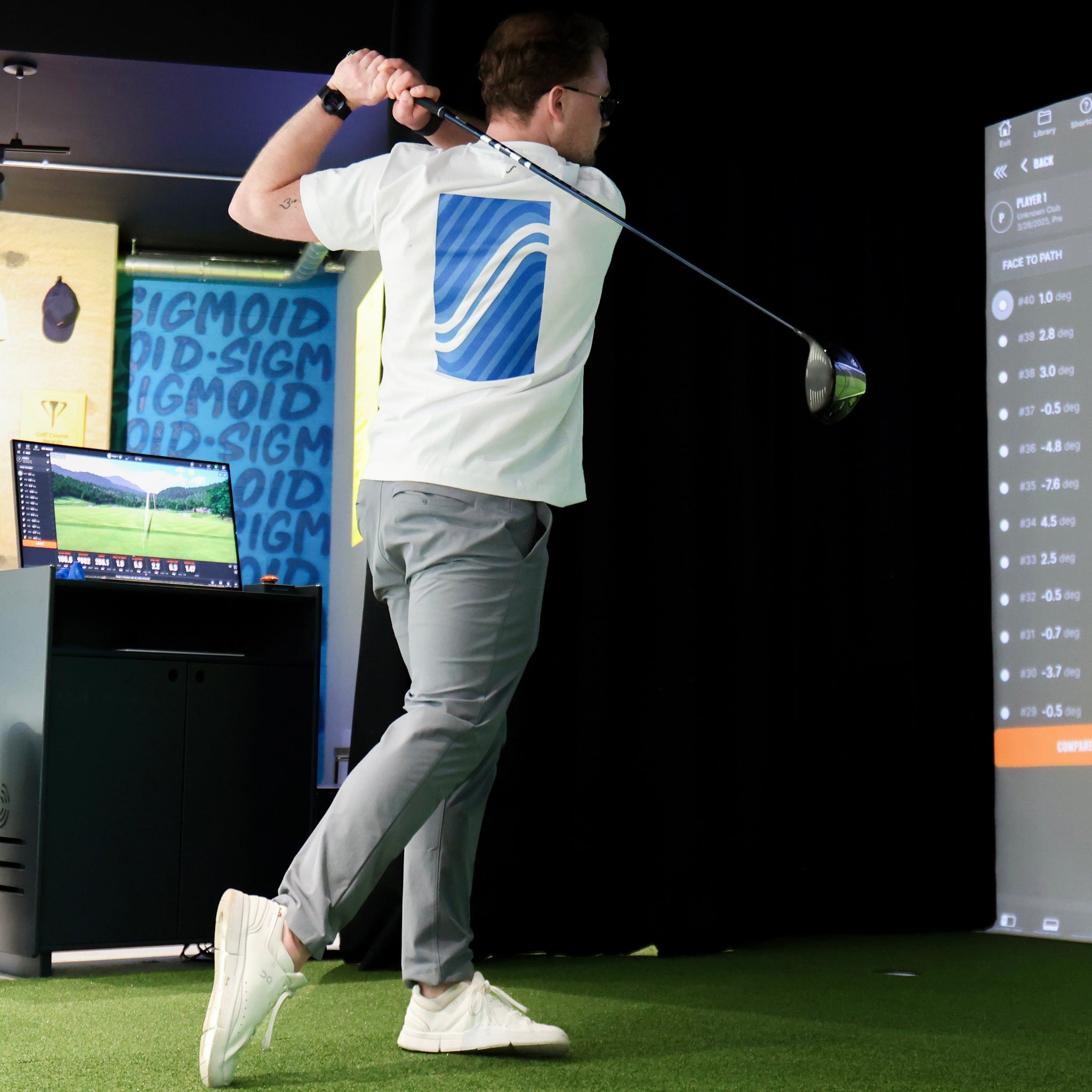 Person playing golf on a simulator with a screen displaying a golf course.
