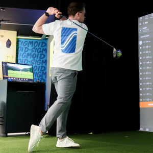 Person playing golf on a simulator with a screen displaying a golf course.