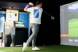 Person playing golf on a simulator with a screen displaying a golf course.