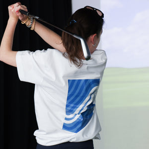 Woman wearing a white shirt with a blue logo, holding a golf club against a golf simulator.
